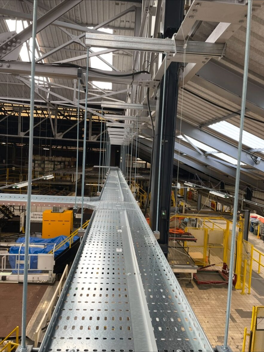 Long high-level cable tray run threaded above a live production floor.